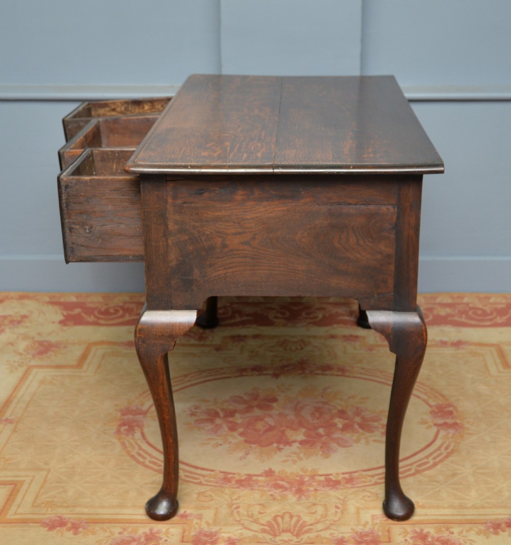 An early 18th-century George I dark oak lowboy featuring three drawers with brass handles, a shaped kneehole apron, and cabriole legs ending in pad feet. View XIV