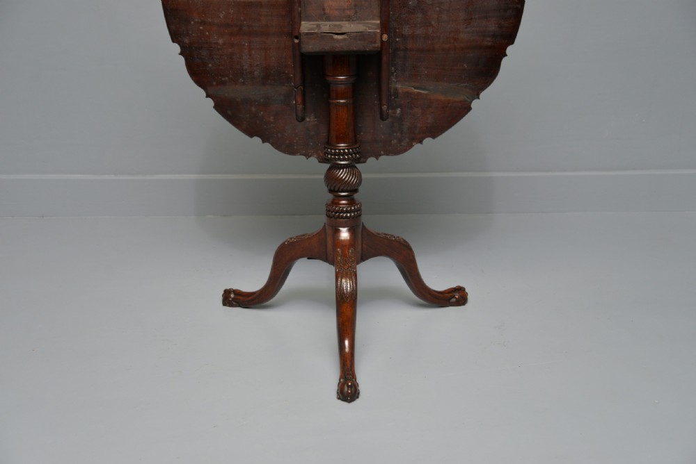 An 18th-century George III mahogany tripod table featuring a circular pie-crust rim, carved turned column, and cabriole legs ending in claw and ball feet. View XVII