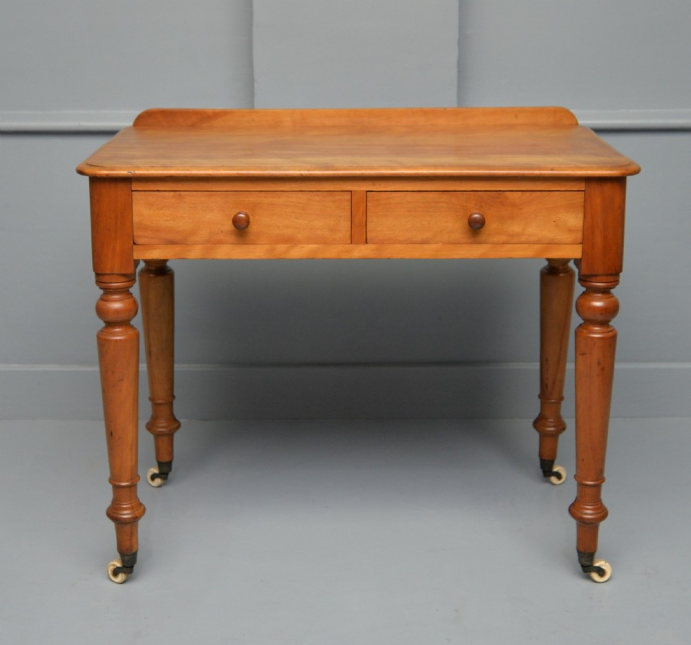 A Victorian satinwood writing table featuring two frieze drawers with wooden knobs, a low rear gallery, turned legs, and ceramic castors.