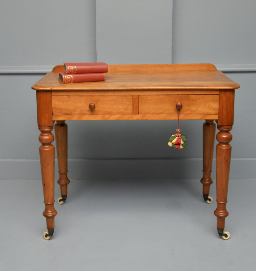 A Victorian satinwood writing table featuring two frieze drawers with wooden knobs, a low rear gallery, turned legs, and ceramic castors. View II