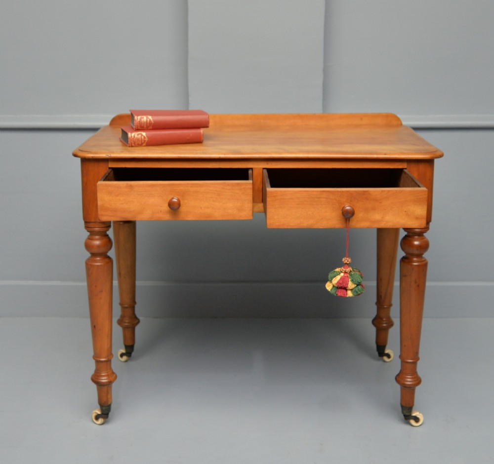 A Victorian satinwood writing table featuring two frieze drawers with wooden knobs, a low rear gallery, turned legs, and ceramic castors. View III