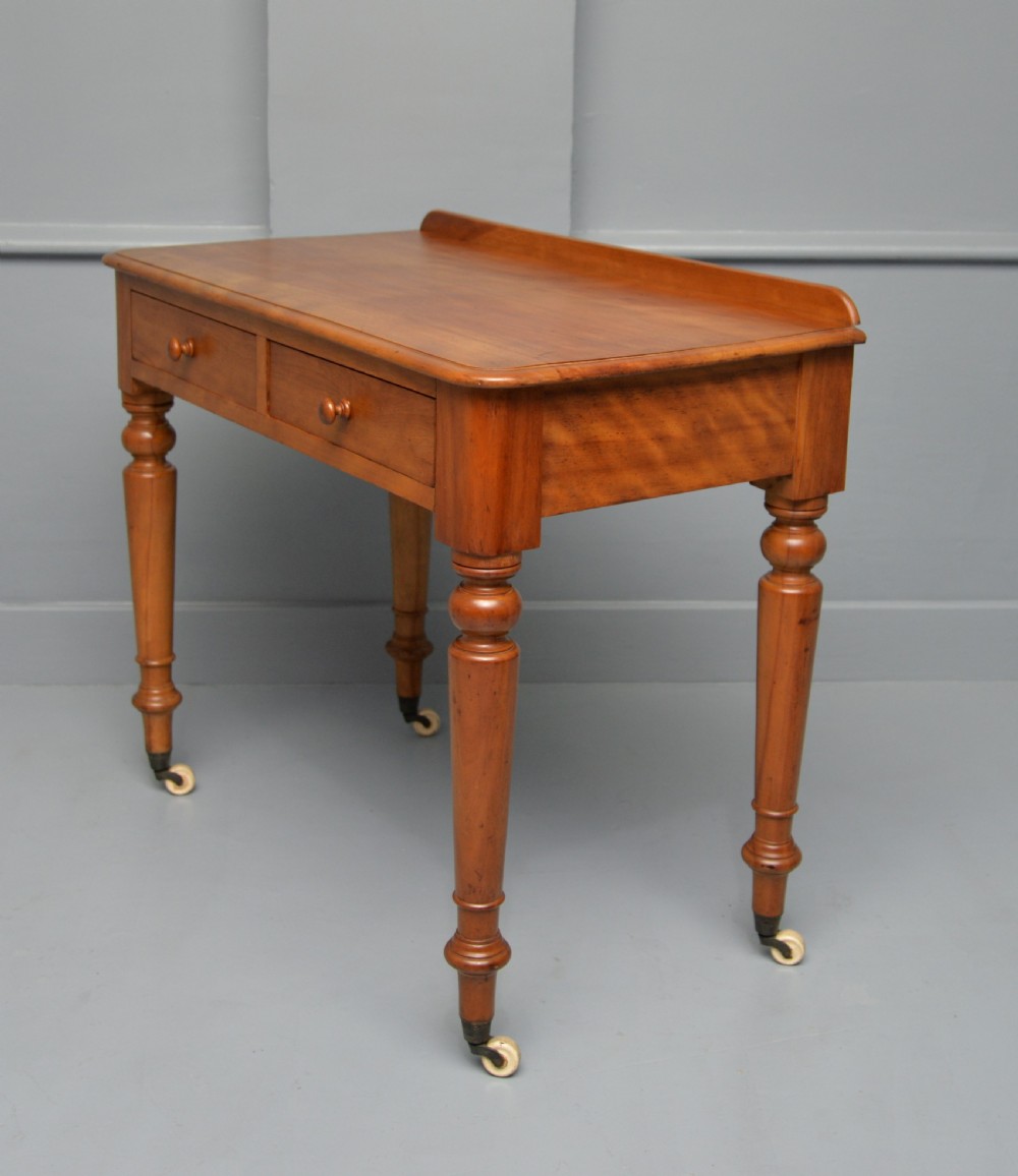 A Victorian satinwood writing table featuring two frieze drawers with wooden knobs, a low rear gallery, turned legs, and ceramic castors. View VII
