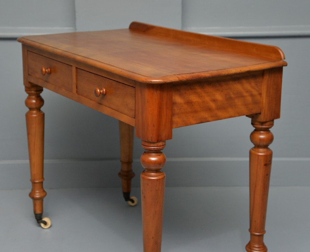 A Victorian satinwood writing table featuring two frieze drawers with wooden knobs, a low rear gallery, turned legs, and ceramic castors. View VIII
