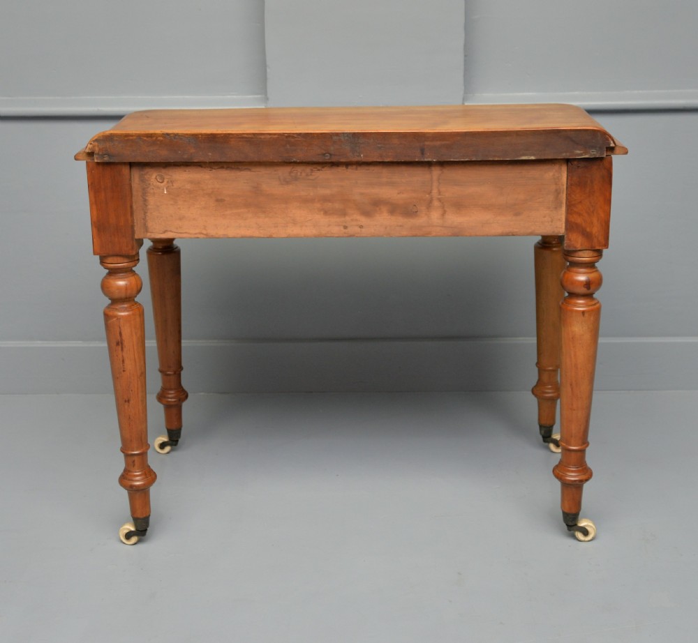 A Victorian satinwood writing table featuring two frieze drawers with wooden knobs, a low rear gallery, turned legs, and ceramic castors. View IX