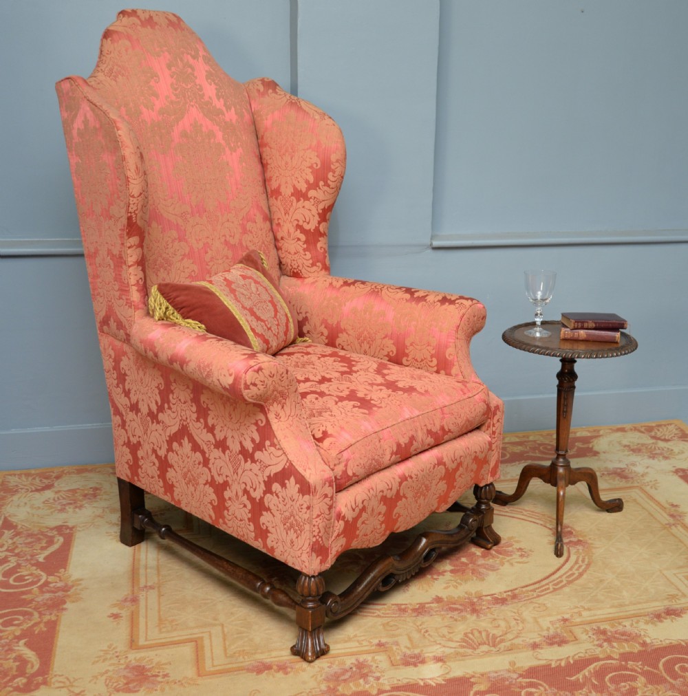 A high-backed wing armchair upholstered in patterned terracotta damask with a matching lumbar cushion and carved dark wood legs. View II