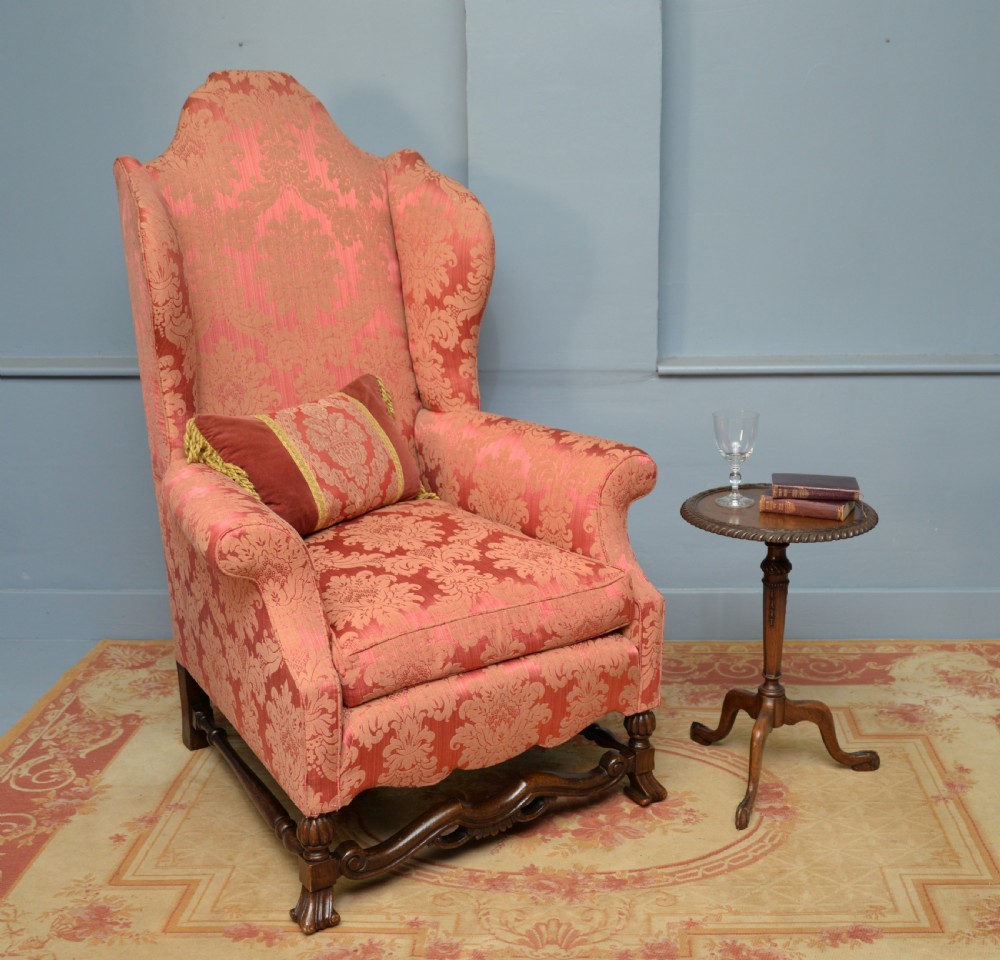 A high-backed wing armchair upholstered in patterned terracotta damask with a matching lumbar cushion and carved dark wood legs. View III