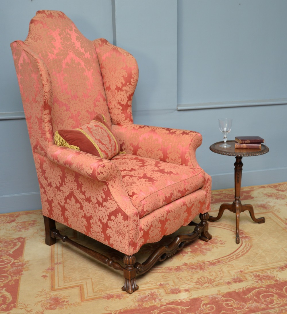 A high-backed wing armchair upholstered in patterned terracotta damask with a matching lumbar cushion and carved dark wood legs. View V