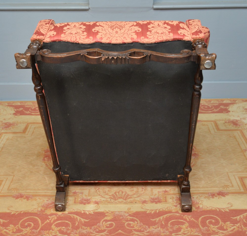 A high-backed wing armchair upholstered in patterned terracotta damask with a matching lumbar cushion and carved dark wood legs. View XXIII