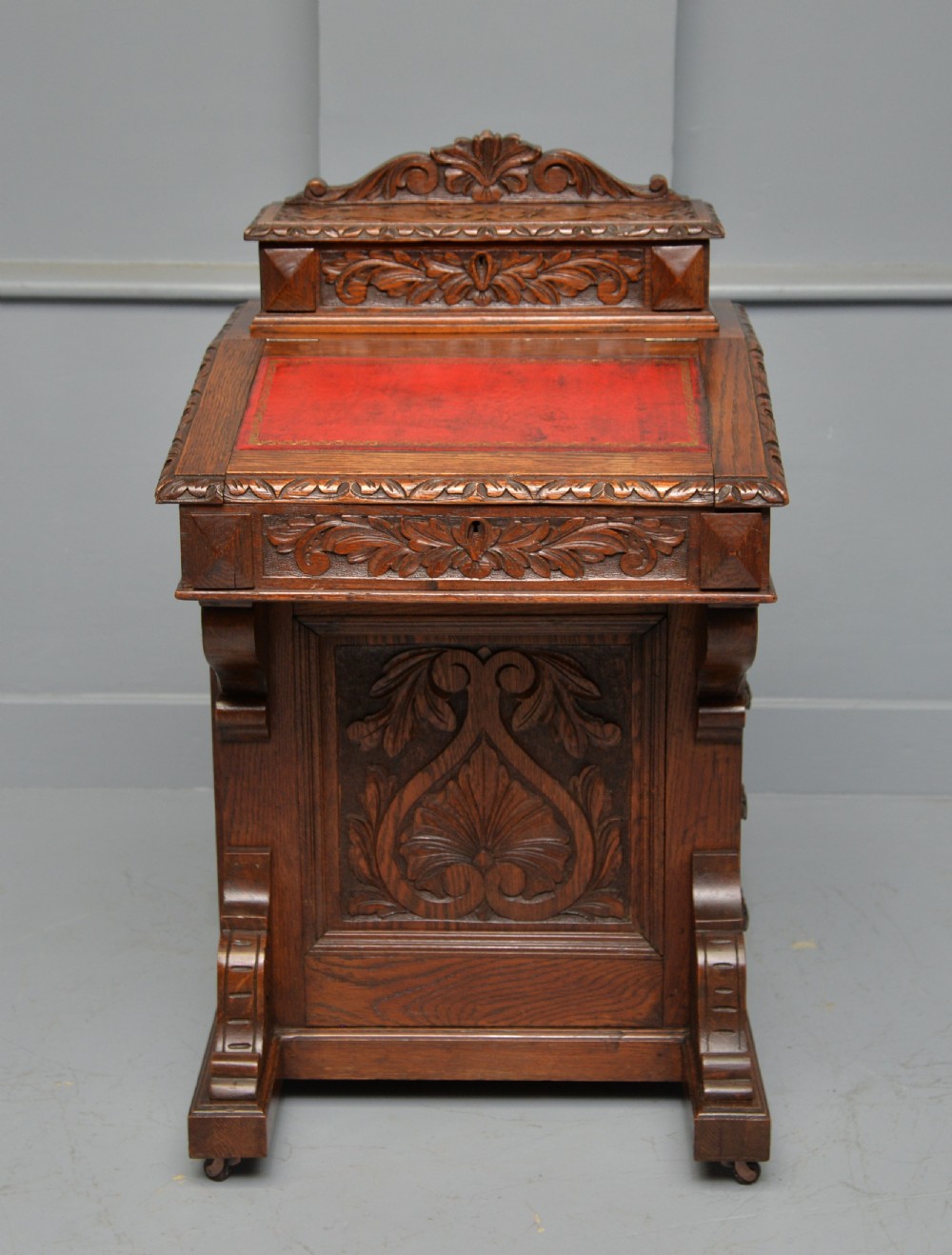 A Victorian dark carved oak Davenport desk featuring a red leather writing slant, carved Green Man mask handles on four side drawers, and a raised stationery gallery. View II