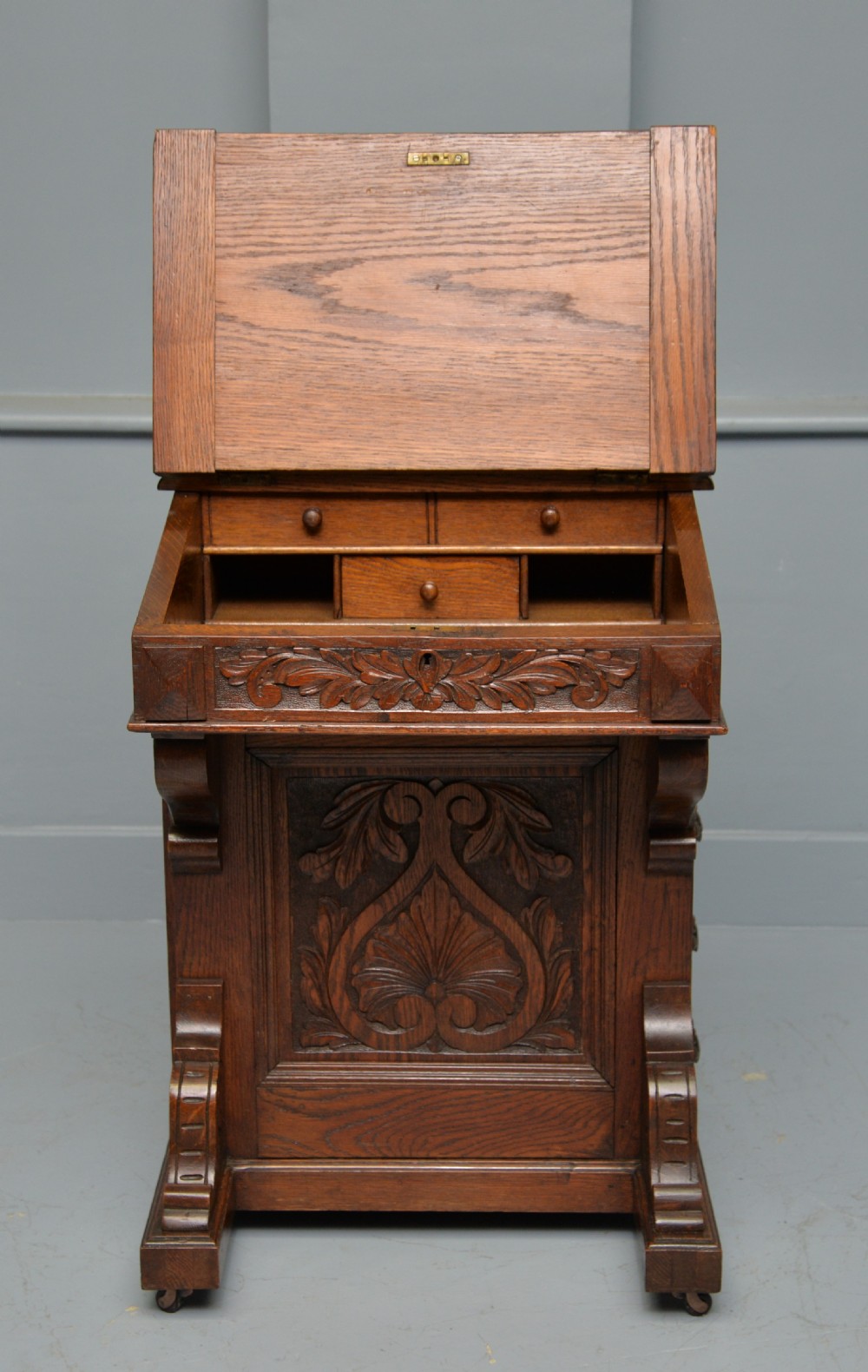 A Victorian dark carved oak Davenport desk featuring a red leather writing slant, carved Green Man mask handles on four side drawers, and a raised stationery gallery. View VIII