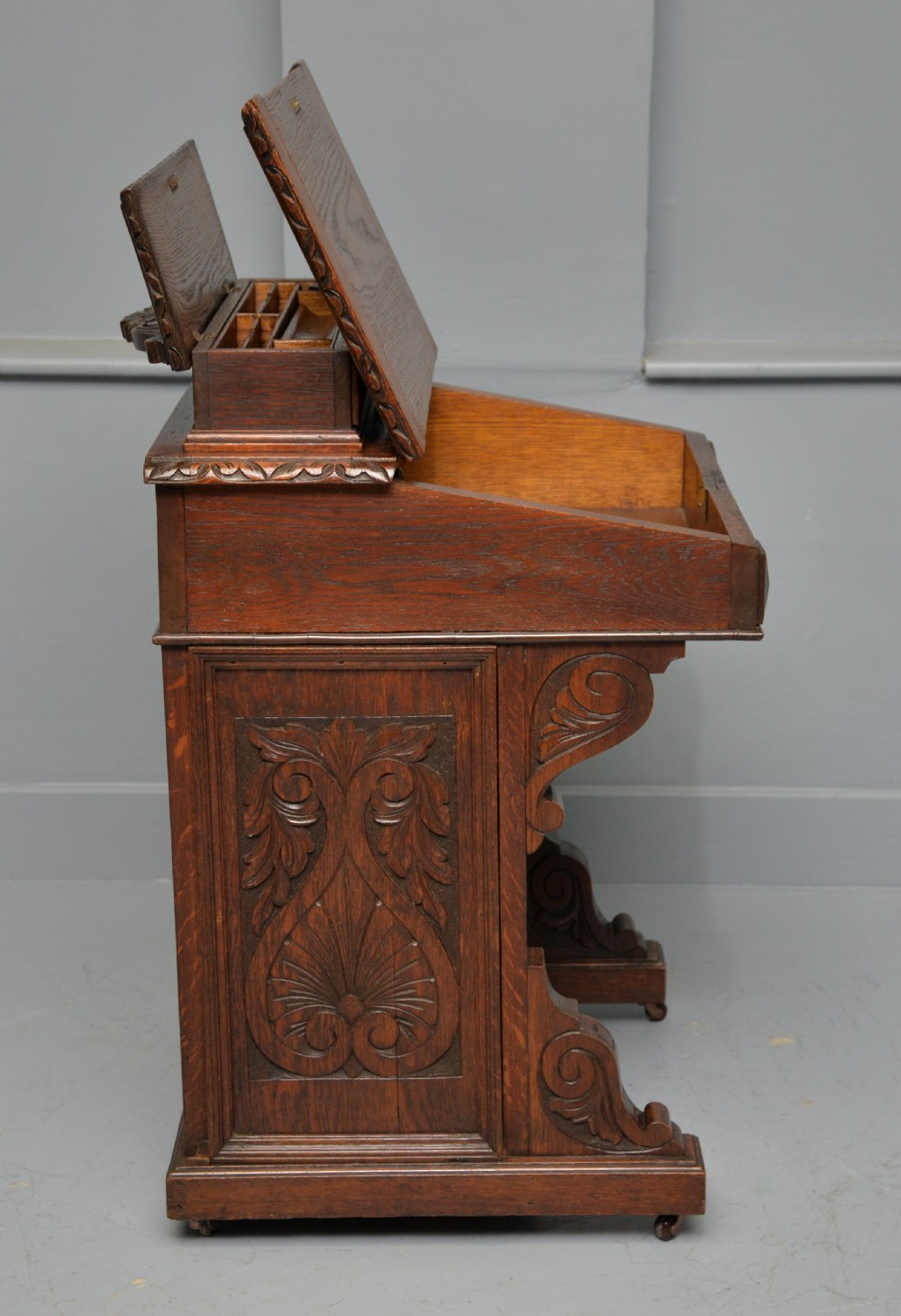A Victorian dark carved oak Davenport desk featuring a red leather writing slant, carved Green Man mask handles on four side drawers, and a raised stationery gallery. View XIII