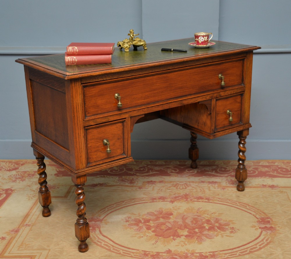 A solid oak writing table featuring a green leather inset top, three drawers with brass drop handles, and turned barley twist legs.