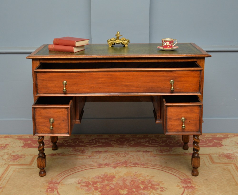 A solid oak writing table featuring a green leather inset top, three drawers with brass drop handles, and turned barley twist legs. View III