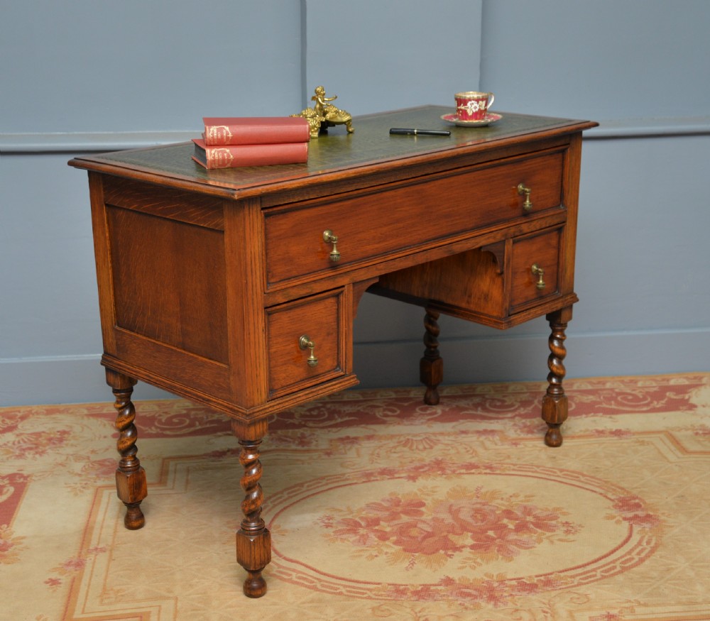 A solid oak writing table featuring a green leather inset top, three drawers with brass drop handles, and turned barley twist legs. View V