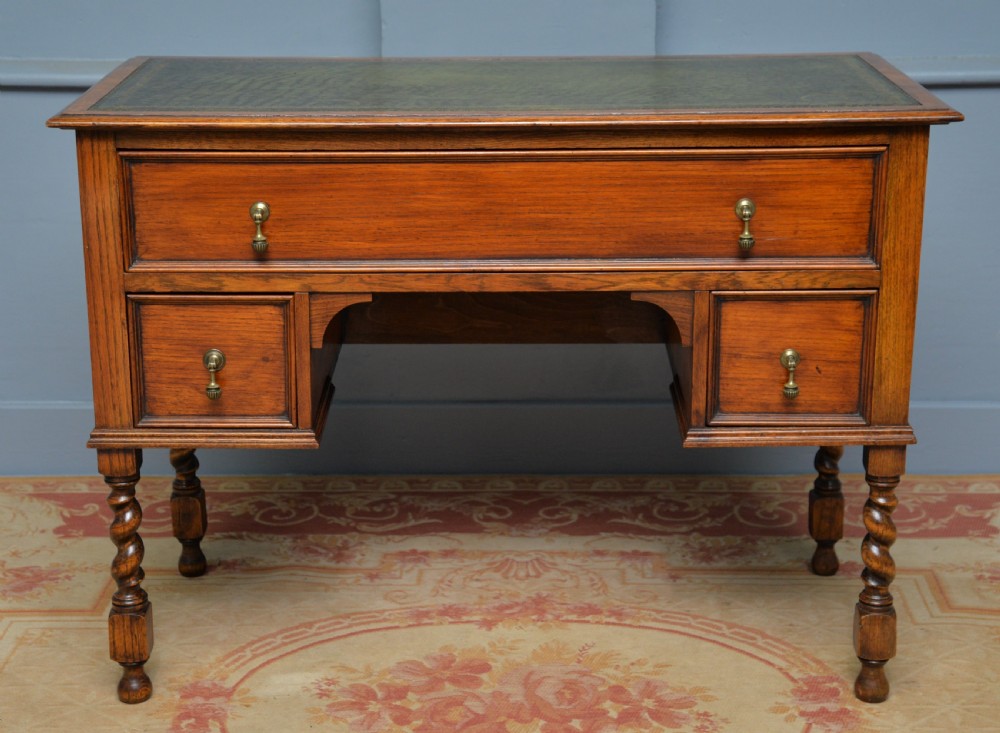 A solid oak writing table featuring a green leather inset top, three drawers with brass drop handles, and turned barley twist legs. View VIII