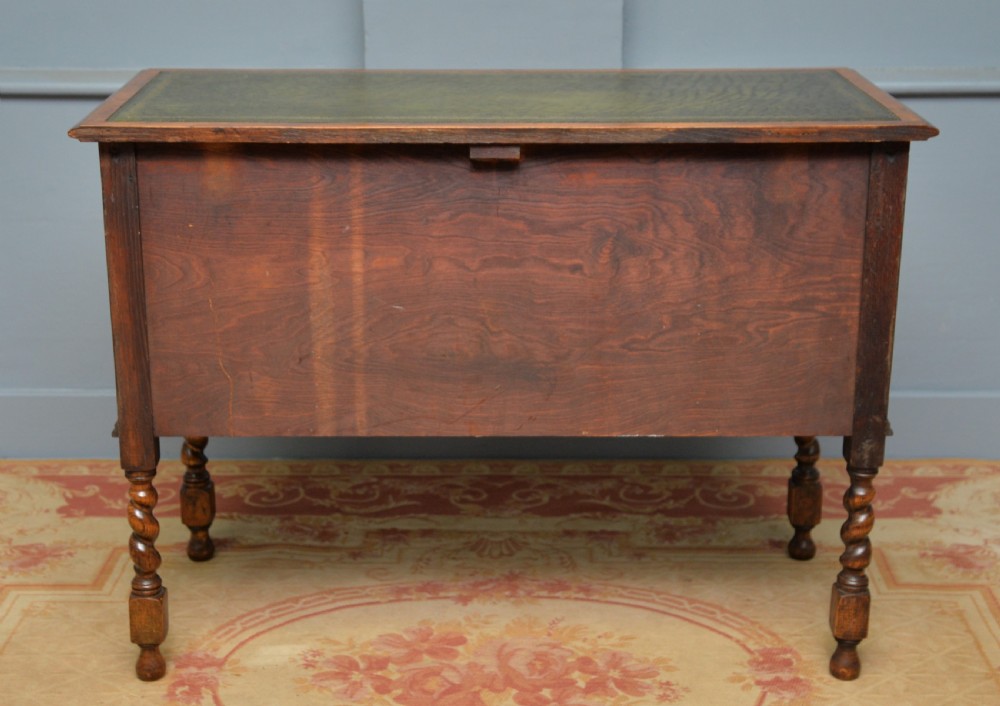 A solid oak writing table featuring a green leather inset top, three drawers with brass drop handles, and turned barley twist legs. View XII
