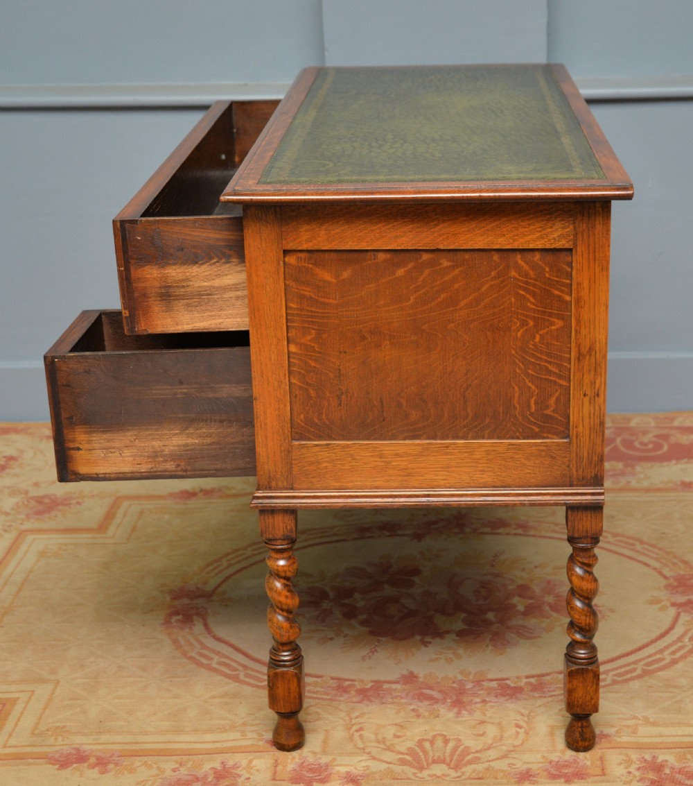 A solid oak writing table featuring a green leather inset top, three drawers with brass drop handles, and turned barley twist legs. View XIII
