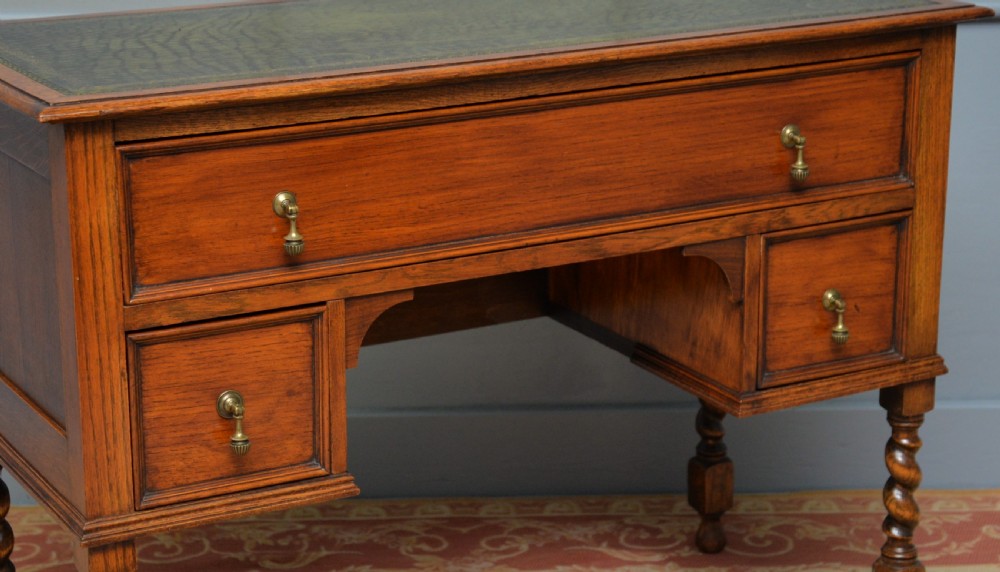 A solid oak writing table featuring a green leather inset top, three drawers with brass drop handles, and turned barley twist legs. View XVII
