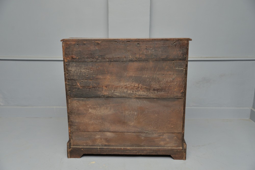 An early 18th-century solid oak writing bureau featuring an angled fall-front that opens to reveal fitted pigeonholes, set over two wide drawers with decorative brass handles. View XII