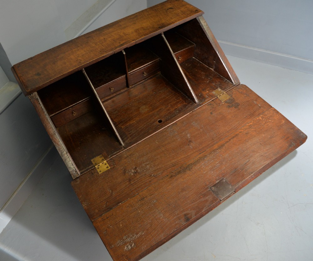 An early 18th-century solid oak writing bureau featuring an angled fall-front that opens to reveal fitted pigeonholes, set over two wide drawers with decorative brass handles. View XV