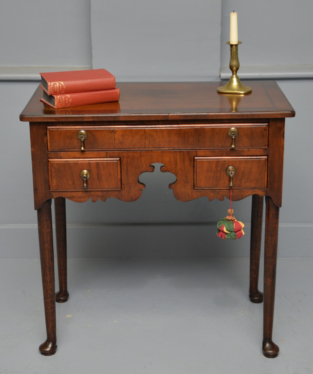 A George II revival walnut lowboy side table featuring three drawers with brass drop handles, a shaped kneehole apron, and slender cabriole legs with pad feet.