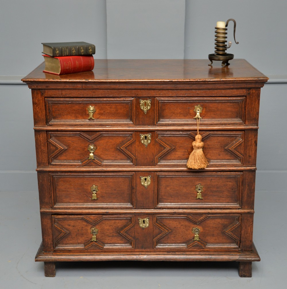 A 17th-century oak chest of drawers featuring geometric panel mouldings across four drawer fronts and brass drop handles.
