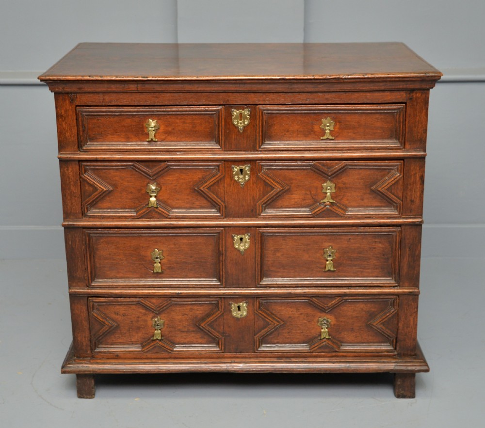 A 17th-century oak chest of drawers featuring geometric panel mouldings across four drawer fronts and brass drop handles. View VI