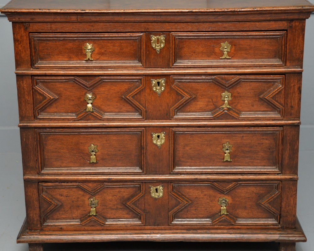 A 17th-century oak chest of drawers featuring geometric panel mouldings across four drawer fronts and brass drop handles. View VIII