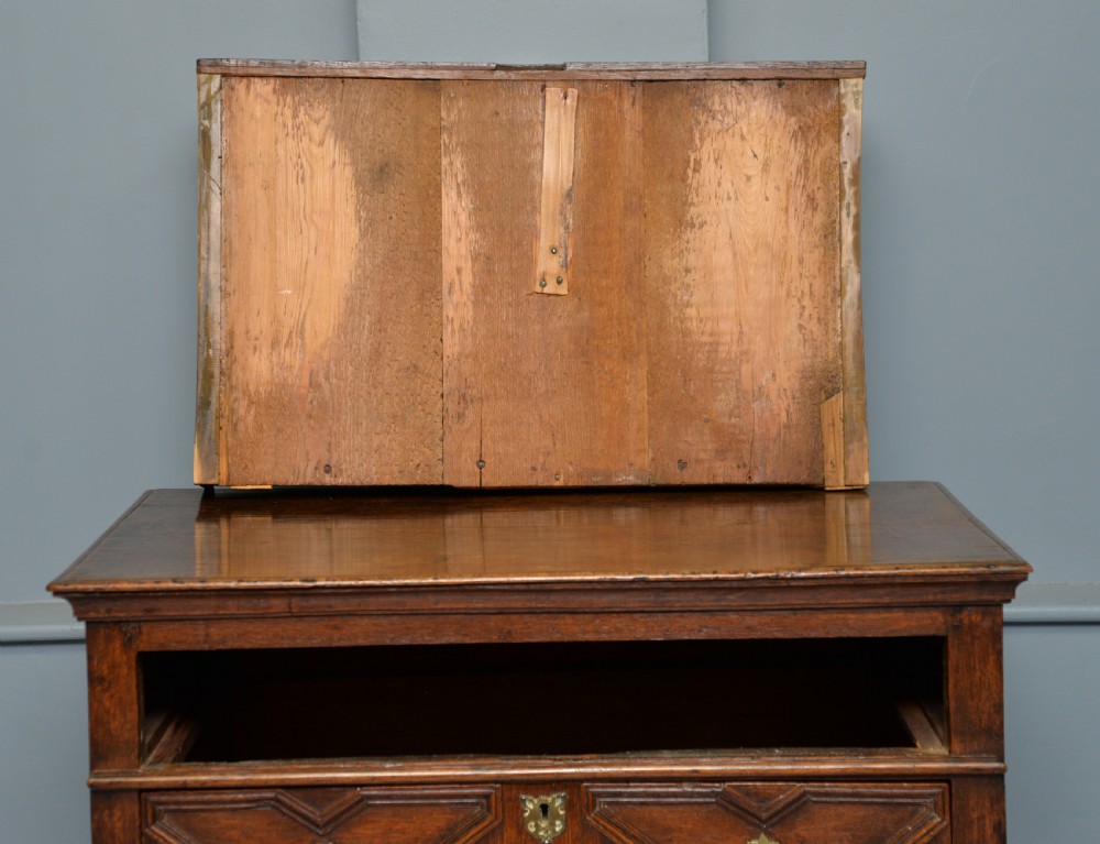 A 17th-century oak chest of drawers featuring geometric panel mouldings across four drawer fronts and brass drop handles. View XVI