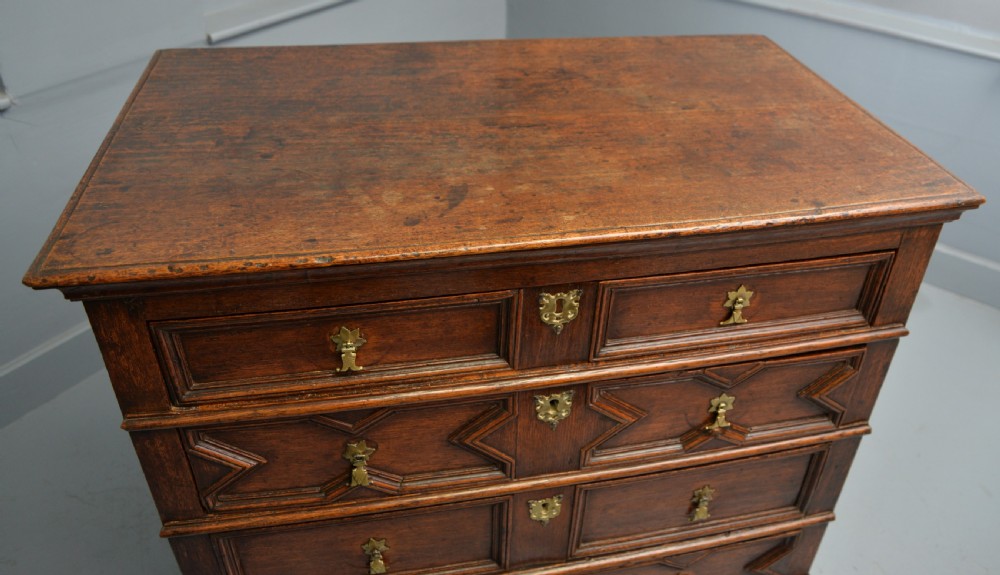 A 17th-century oak chest of drawers featuring geometric panel mouldings across four drawer fronts and brass drop handles. View XVIII