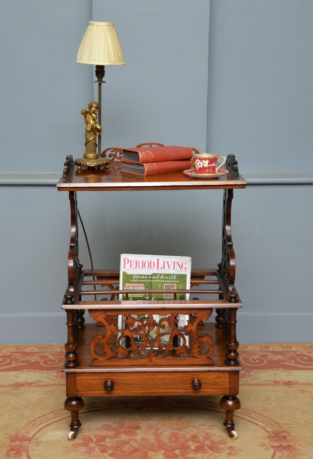 A Victorian burr walnut Canterbury table featuring a top shelf with pierced fretwork, lower magazine compartments, a single drawer, and turned legs with ceramic castors. View III