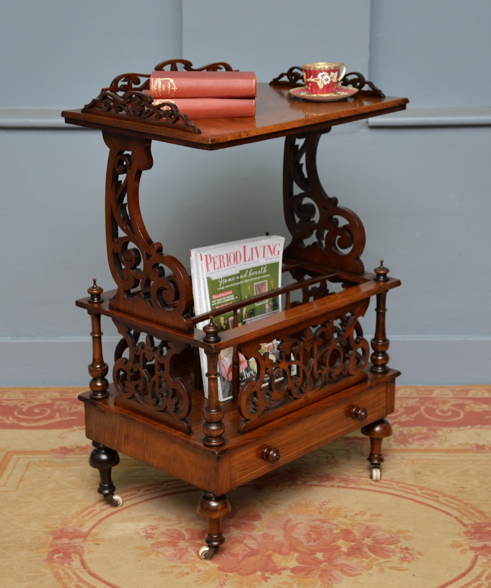 A Victorian burr walnut Canterbury table featuring a top shelf with pierced fretwork, lower magazine compartments, a single drawer, and turned legs with ceramic castors. View V