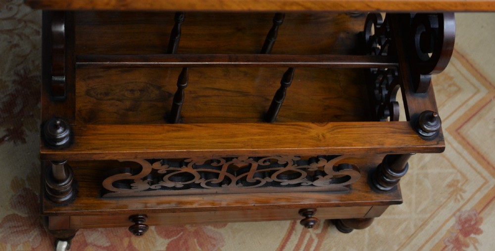 A Victorian burr walnut Canterbury table featuring a top shelf with pierced fretwork, lower magazine compartments, a single drawer, and turned legs with ceramic castors. View XV