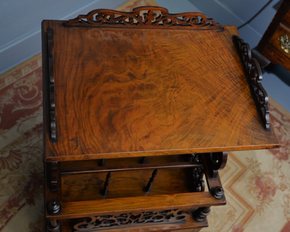 A Victorian burr walnut Canterbury table featuring a top shelf with pierced fretwork, lower magazine compartments, a single drawer, and turned legs with ceramic castors. View XVI