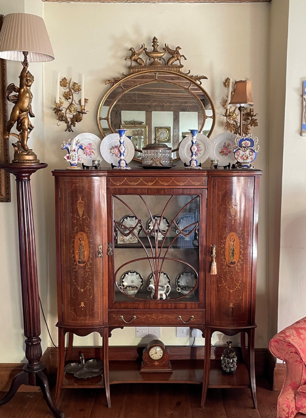 An inlaid mahogany display cabinet featuring a central glazed door with curved astragal glazing bars, flanking curved inlaid cupboard doors, a lower drawer, and an undertier shelf. View II