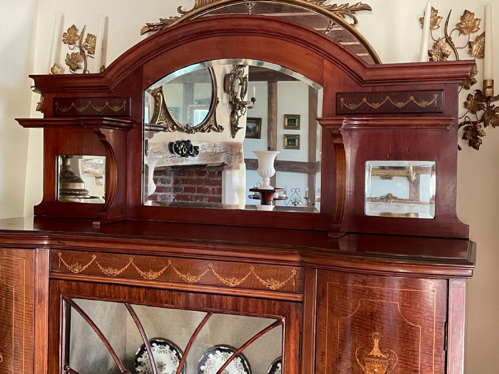 An inlaid mahogany display cabinet featuring a central glazed door with curved astragal glazing bars, flanking curved inlaid cupboard doors, a lower drawer, and an undertier shelf. View XII
