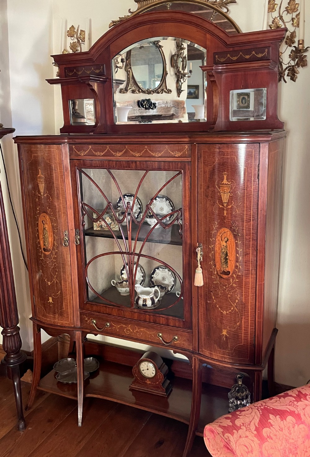 An inlaid mahogany display cabinet featuring a central glazed door with curved astragal glazing bars, flanking curved inlaid cupboard doors, a lower drawer, and an undertier shelf. View XIII