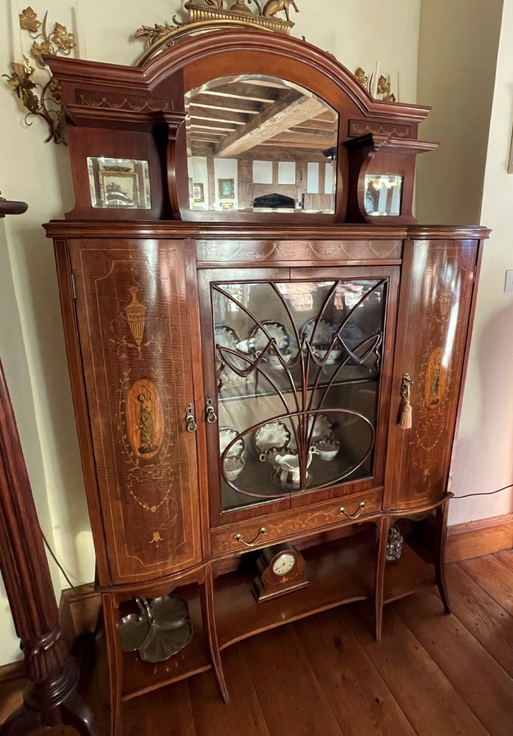 An inlaid mahogany display cabinet featuring a central glazed door with curved astragal glazing bars, flanking curved inlaid cupboard doors, a lower drawer, and an undertier shelf. View XX