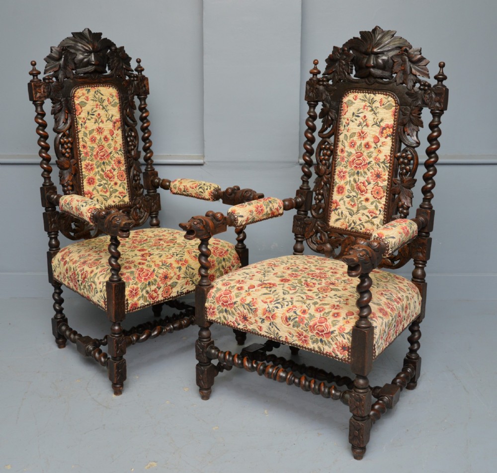A pair of Victorian dark oak throne chairs featuring Green Man carved crestings, barley twist supports, carved beast armrests, and floral pattern upholstery.