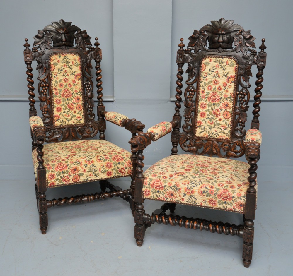 A pair of Victorian dark oak throne chairs featuring Green Man carved crestings, barley twist supports, carved beast armrests, and floral pattern upholstery. View II