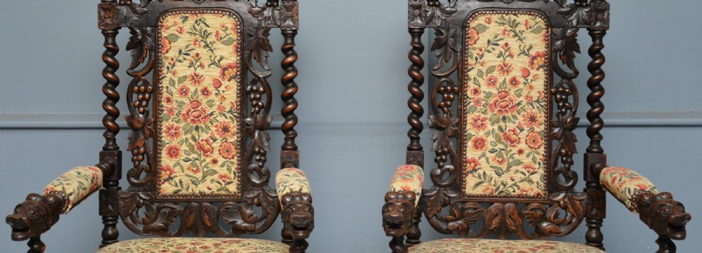 A pair of Victorian dark oak throne chairs featuring Green Man carved crestings, barley twist supports, carved beast armrests, and floral pattern upholstery. View VII
