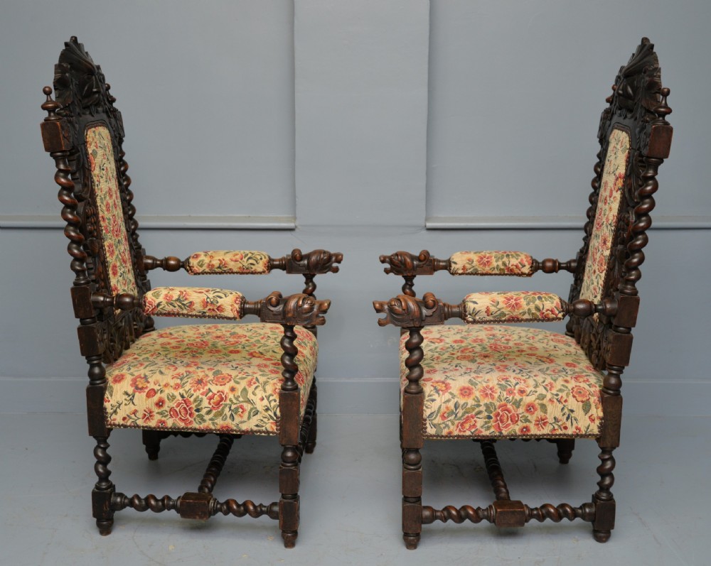 A pair of Victorian dark oak throne chairs featuring Green Man carved crestings, barley twist supports, carved beast armrests, and floral pattern upholstery. View IX