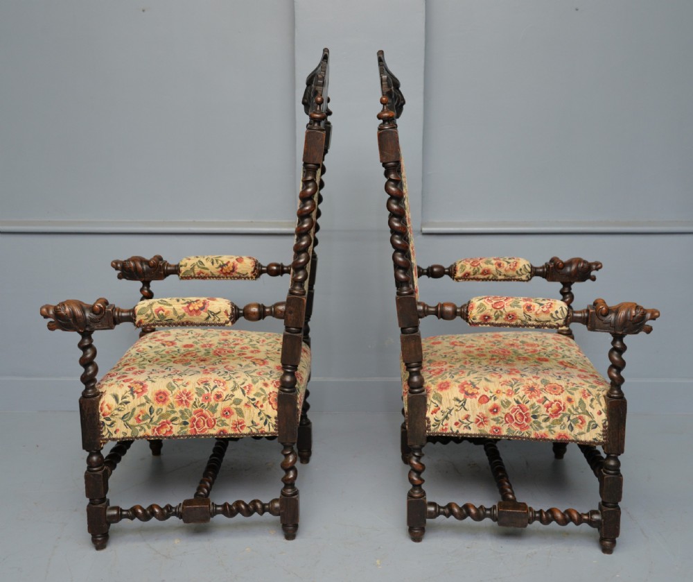 A pair of Victorian dark oak throne chairs featuring Green Man carved crestings, barley twist supports, carved beast armrests, and floral pattern upholstery. View XII