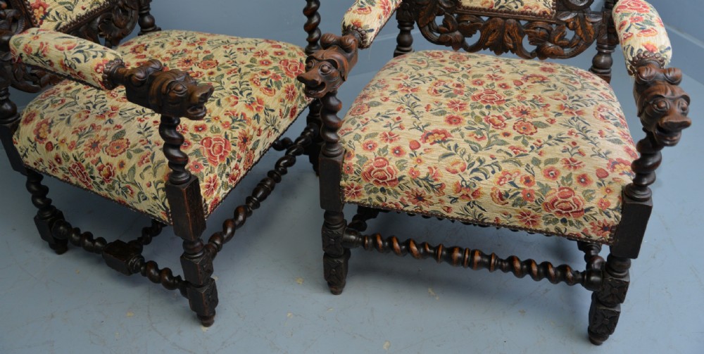 A pair of Victorian dark oak throne chairs featuring Green Man carved crestings, barley twist supports, carved beast armrests, and floral pattern upholstery. View XIII
