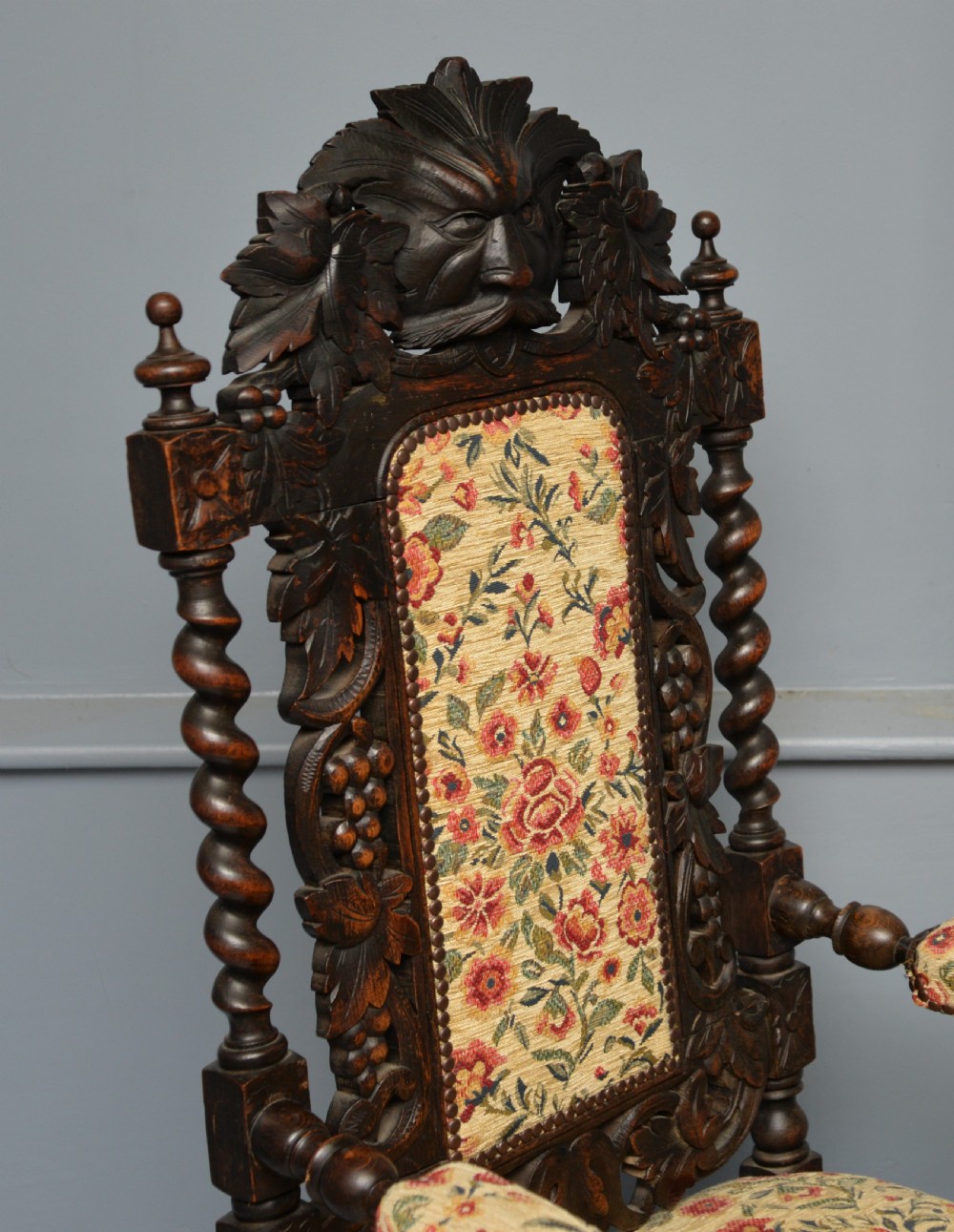 A pair of Victorian dark oak throne chairs featuring Green Man carved crestings, barley twist supports, carved beast armrests, and floral pattern upholstery. View XIV