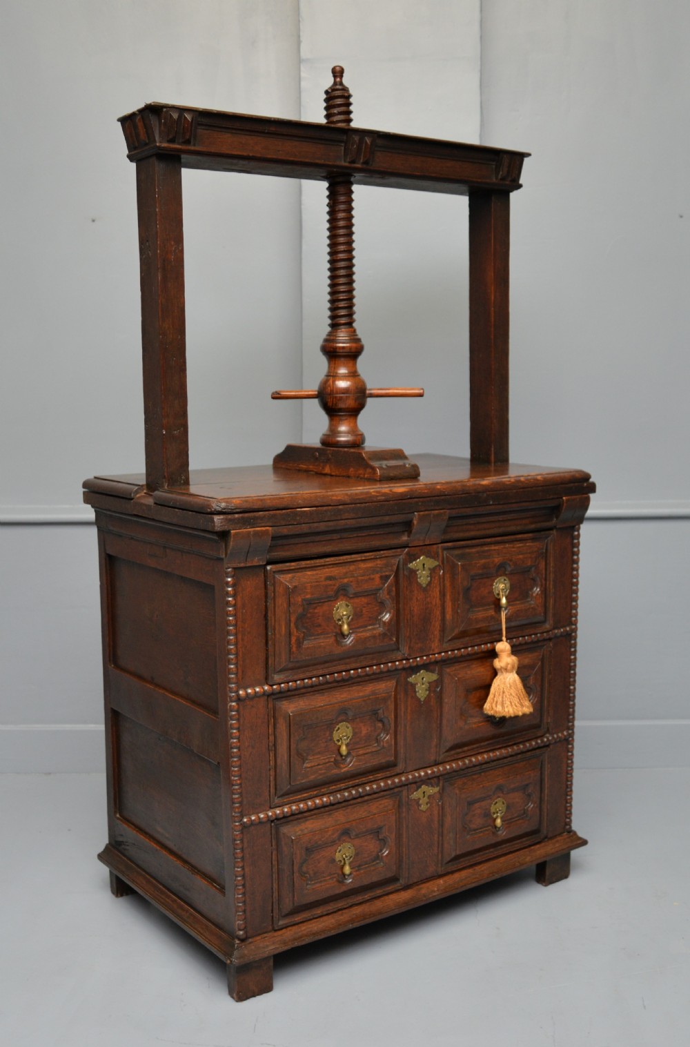 A 17th-century dark oak chest of drawers featuring geometric panelled drawer fronts and an integrated wooden screw linen press mounted on top.