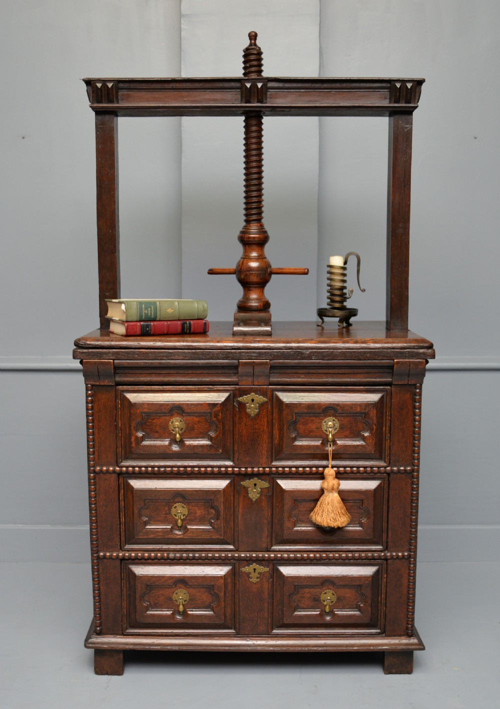 A 17th-century dark oak chest of drawers featuring geometric panelled drawer fronts and an integrated wooden screw linen press mounted on top. View II
