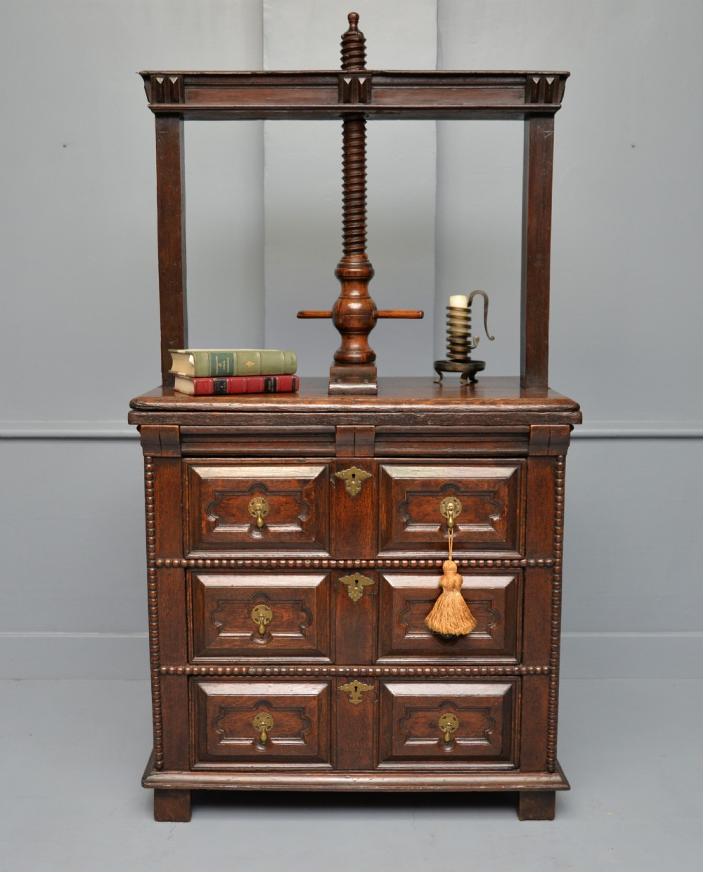 A 17th-century dark oak chest of drawers featuring geometric panelled drawer fronts and an integrated wooden screw linen press mounted on top. View III