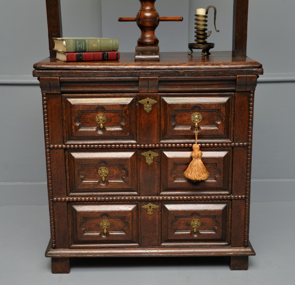 A 17th-century dark oak chest of drawers featuring geometric panelled drawer fronts and an integrated wooden screw linen press mounted on top. View V