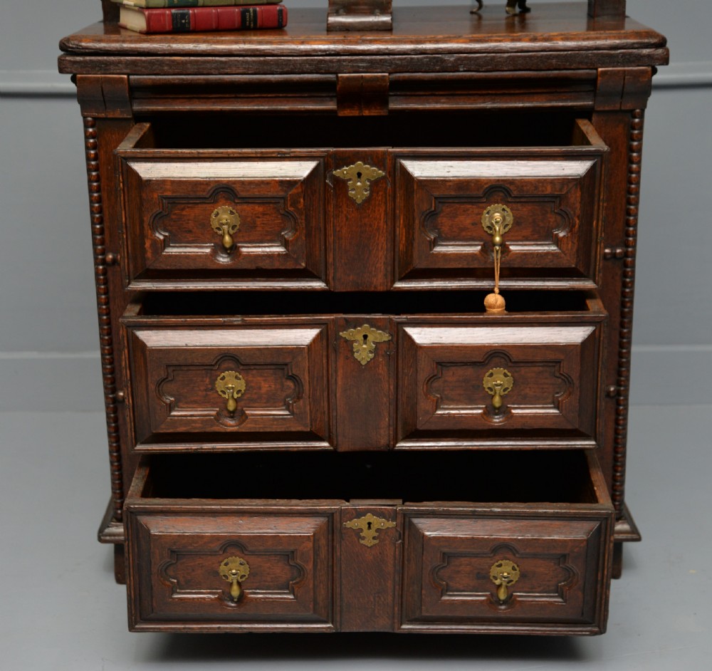 A 17th-century dark oak chest of drawers featuring geometric panelled drawer fronts and an integrated wooden screw linen press mounted on top. View VI